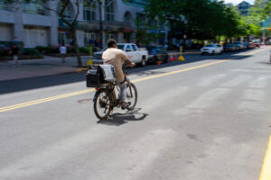 Delivery man on e-bike travels along street.